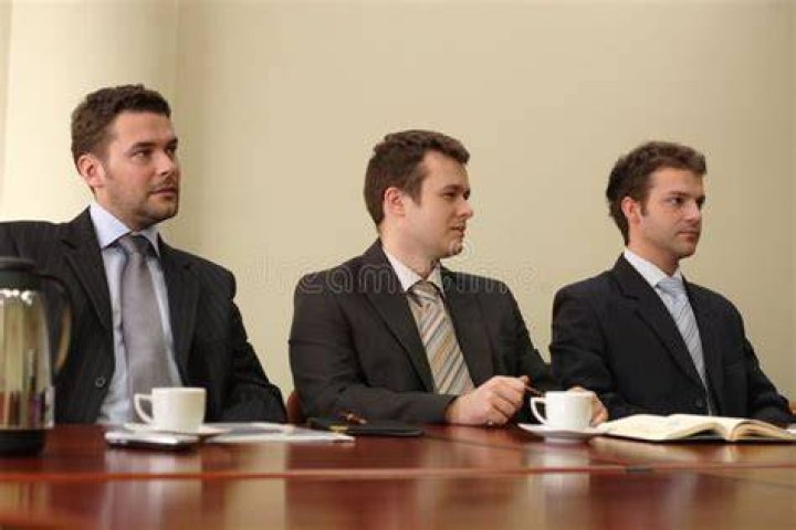 Three men in suits sitting in armchairs and smiling.